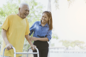 Younger woman helps older man walk with walker.