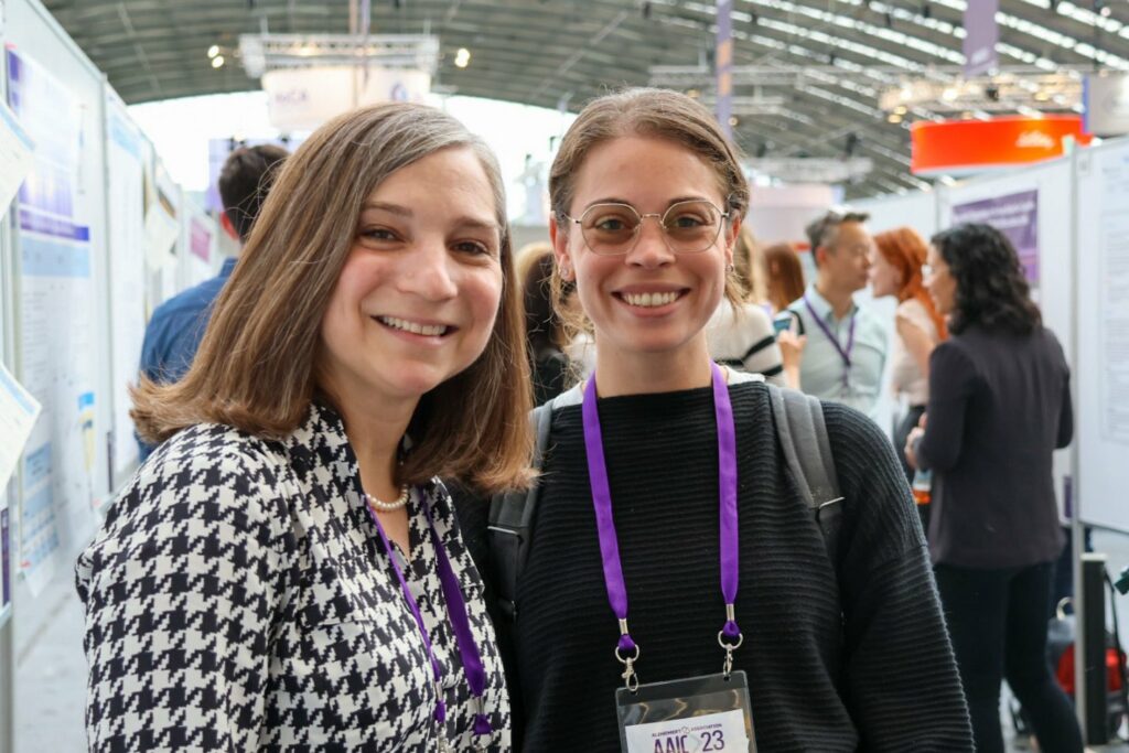 Two women smile at the camera in a conference hall.